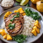 Grilled pork loin chops with a sticky mango glaze served with fluffy coconut rice, garnished with fresh cilantro and lime wedges.